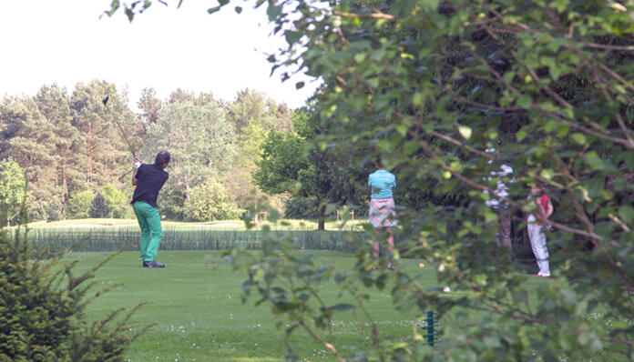 Ein Golfer schlägt einen Ball ab, während drei andere Personen zuschauen.