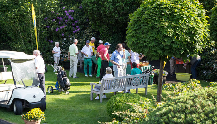 Golfer:innnen unterhalten sich in einem Parkbereich mit Sitzbänken.